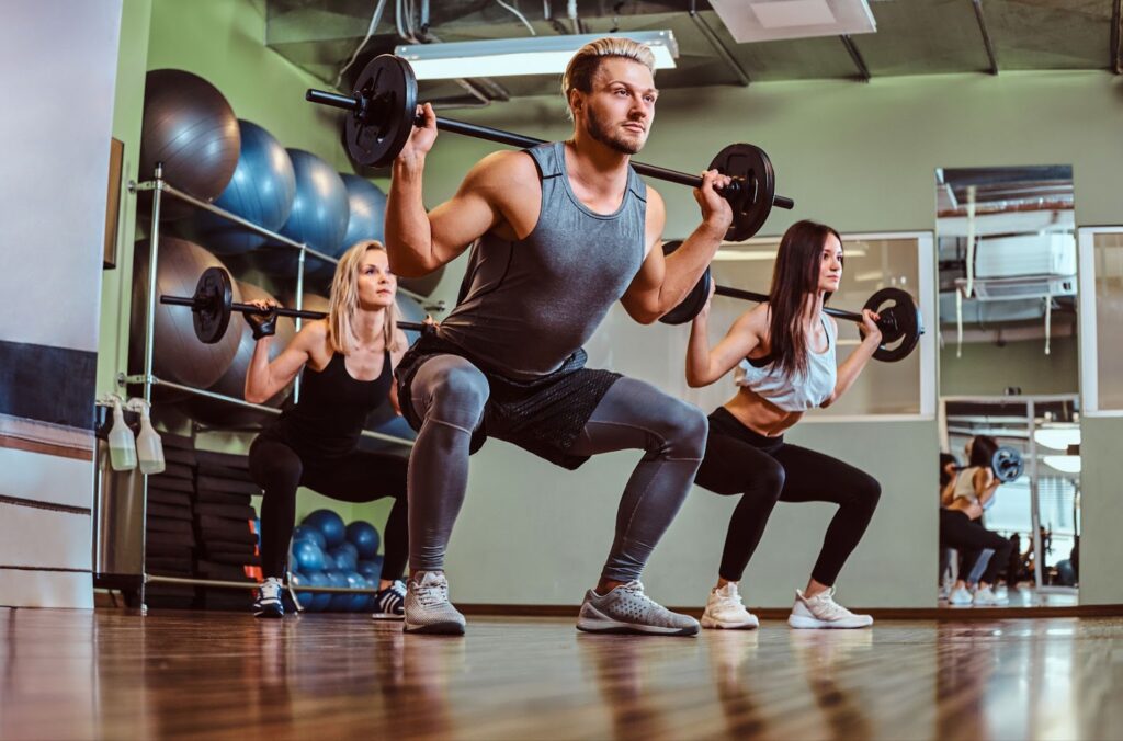 Group of people exercising with barbell doing squats in the fitness club