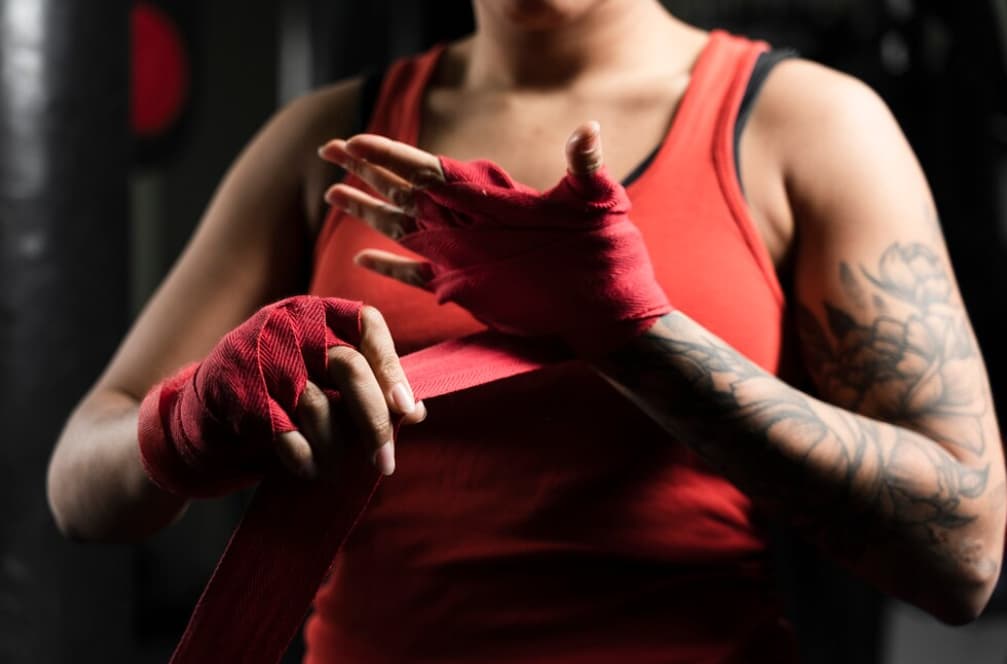 A woman with a tattoo binds her hands with red cloth in the gym